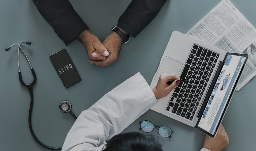 medical doctor pointing to something on a lap top computer screen online to patient