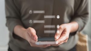 Hands holding a smartphone with translucent floating chat bubbles and user icons, illustrating messaging.
